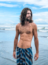 Mid adult shirtless man standing at beach against sky