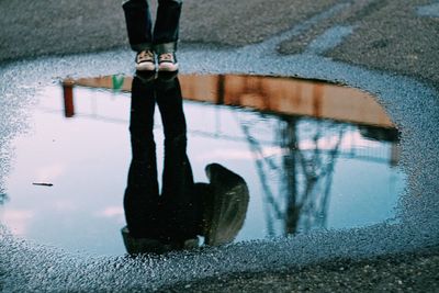 Low section of person reflecting on puddle at road