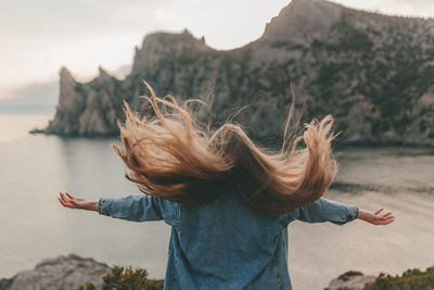 Young girl with long hair in a denim jacket against the backdrop of a mountain landscape