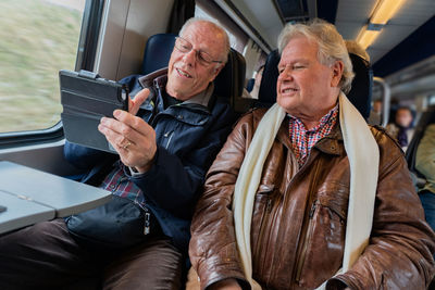 Smiling senior friends taking selfie while sitting in train