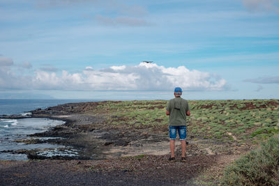 Rear view of man standing on beach against sky