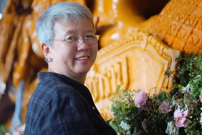 Smiling mature woman by decorated carvings at workshop