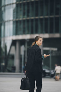 Businesswoman looking over shoulder while walking on street in city