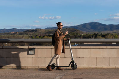 Side view of man going to work on electric scooter with backpack and coffee to go on and landscape