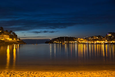 Illuminated buildings by sea against sky at night