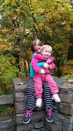 Portrait of sisters sitting on stone wall against trees