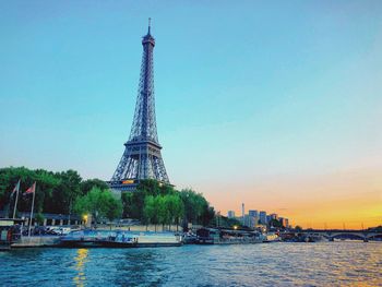 Eiffel tower by river against sky during sunset