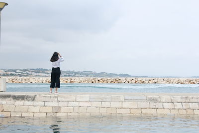 Rear view of woman standing on groyne amidst sea against sky