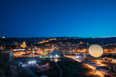 Illuminated cityscape against clear blue sky at night