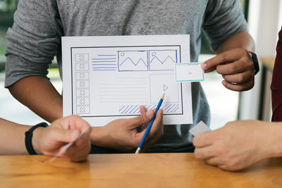 Midsection of man holding paper while sitting on table