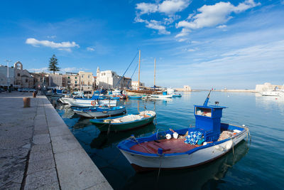 Sailboats moored in harbor by city against sky