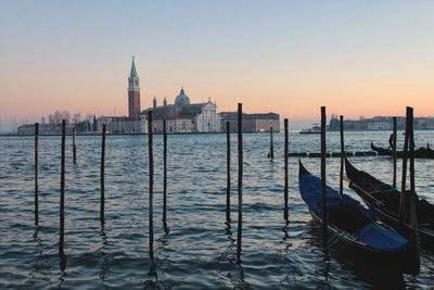 Gondolas moored at canal against sky during sunset