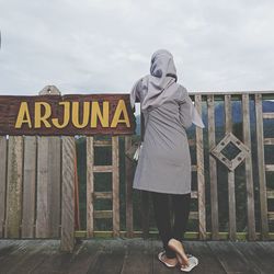 Full length of woman standing by sign against sky