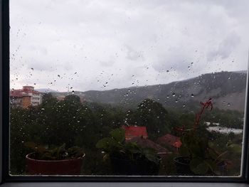 Raindrops on glass window against sky during rainy season