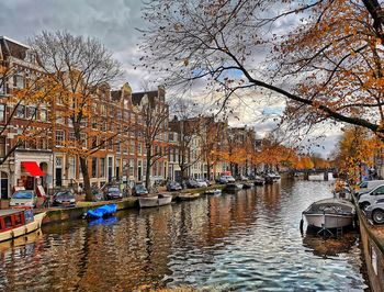 Boats moored in canal by buildings in city during autumn