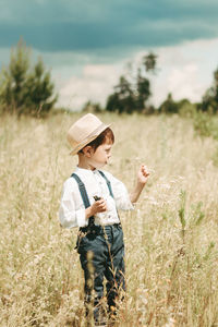 Little farmer on a summer field, cute little boy in a straw hat. boy with a flower 