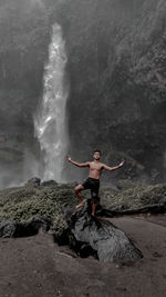 Full length of man standing on rock against waterfall