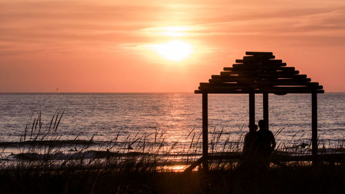 Silhouette man by sea against sky during sunset