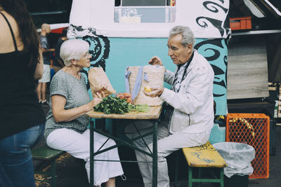 Senior man and woman discussing vegetables while sitting at market in city