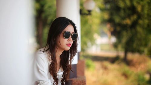 Young woman wearing sunglasses looking away sitting outdoors