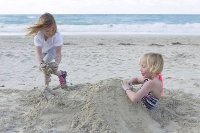 Siblings playing with sand at beach