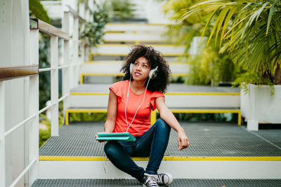 Woman with curly hair holding digital tablet while sitting on steps