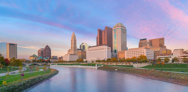 Buildings by river against sky in city