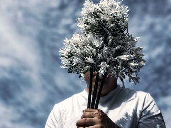 Close-up of man holding bouquet of white flowers against cloudy sky.