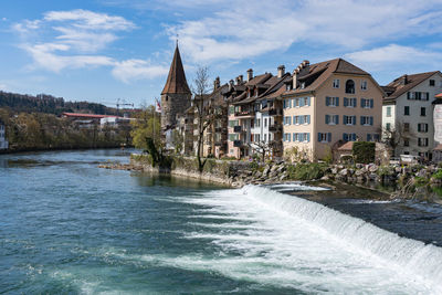 Buildings by river against cloudy sky