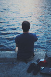 Rear view of man sitting on pier against sea