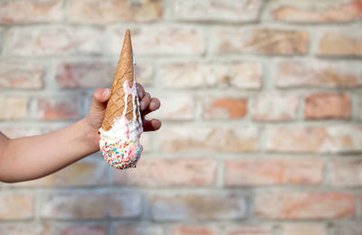 Close-up of hand holding ice cream against wall