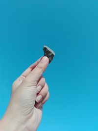Cropped image of hand holding stone against clear blue sky