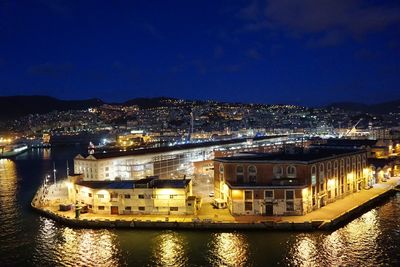 Illuminated buildings by sea against sky at night