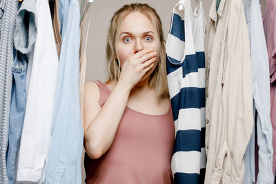 Depressed woman, covers her mouth with her hand with bulging eyes standing in a closet full of