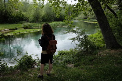 Rear view of girl with backpack standing by lake in park