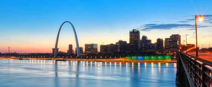 Illuminated buildings by river against sky in city