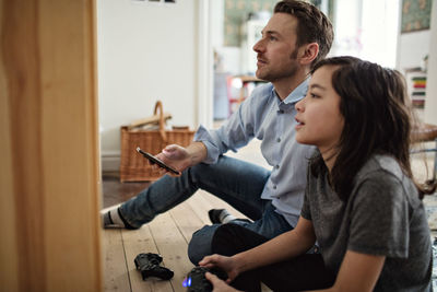 Side view of happy son looking away while playing video game by father in living room