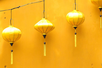 Three yellow lanterns in a row against a yellow wall