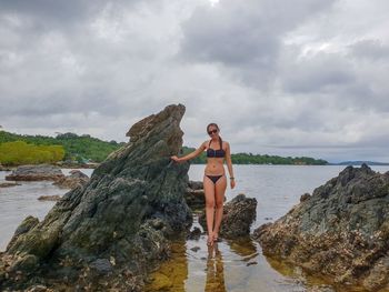 Woman standing on rock by sea against sky