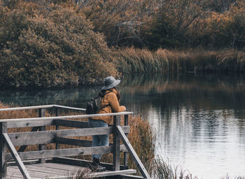 Young woman standing on wooden deck by lake in autumn