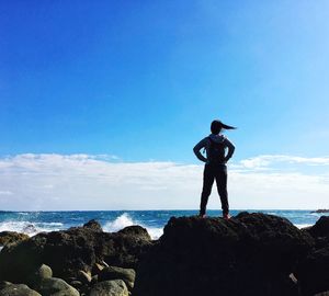 Rear view of woman standing on rock against sea