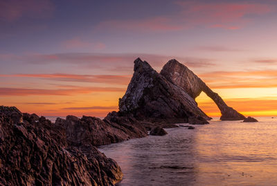 Rock formation in sea against sky during sunset