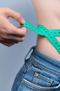 Waist of a slim woman in jeans. close-up of a slim woman measuring the size of her waist with a tape