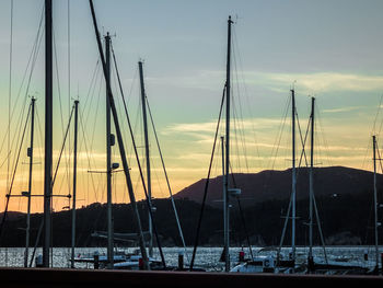 Sailboats moored at harbor against sky during sunset