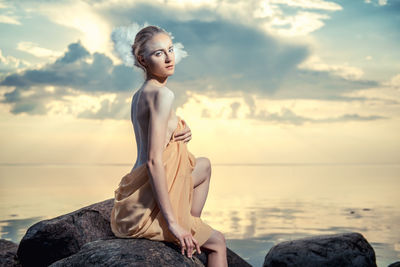 Young woman standing on rock against sea at sunset