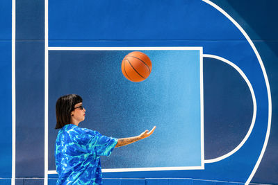 Caucasian girl with sunglasses and tattoos on a blue background with a basketball