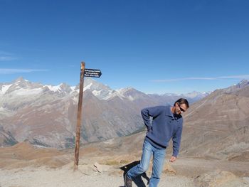 Man walking by information sign on mountain against sky