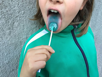 Midsection of girl eating lollipop while standing against wall