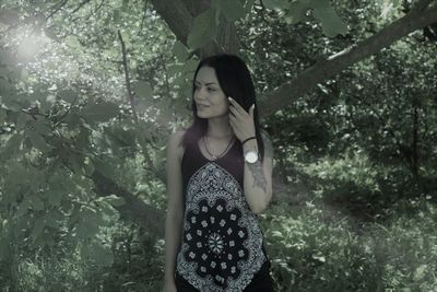 Beautiful smiling young woman with hand in hair standing against trees