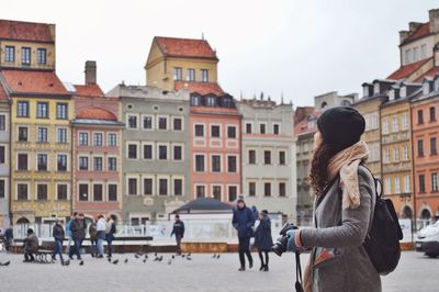 Side view of young woman wearing warm clothing with camera standing on city street